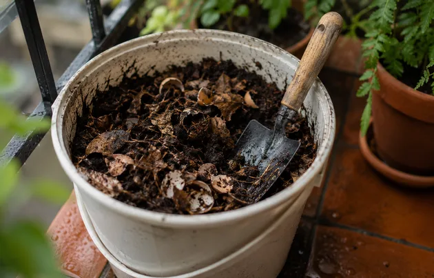Balde de compostagem com adubo orgânico pronto, casca de ovo e pá de jardinagem