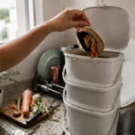 Composteira de baldes empilhados em cozinha de apartamento pequeno, mao jogando restos de vegetais